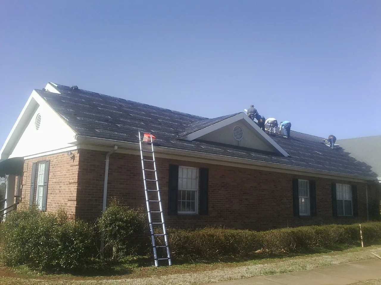 Crew tearing shingles off a brick ranch roof with a ladder set — Metal Roof Repair work by our crew in Loxley