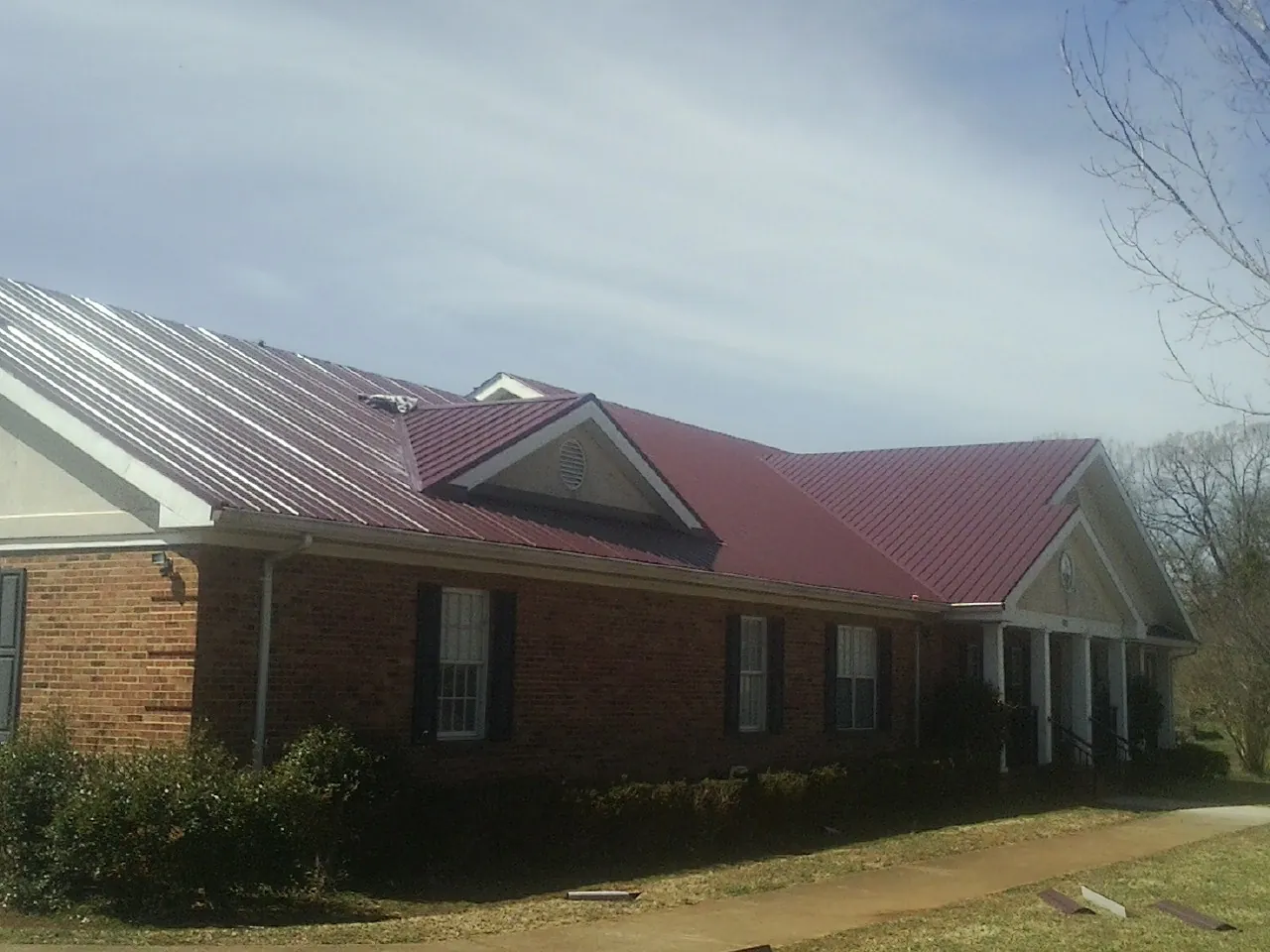Red metal roof with gabled entries on a long brick building, from a Hail Damage Roof Repair job in Loxley