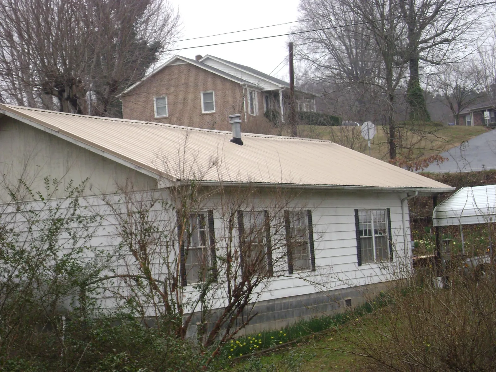 Tan metal roof on a white sided house set into a hillside — Commercial Roofing by Roofing Brothers in Loxley